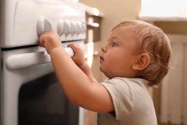 Little child playing with gas stove indoors. Dangers in kitchen