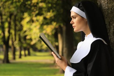 Güneşli bir günde parkta İncil okuyan genç bir rahibe.