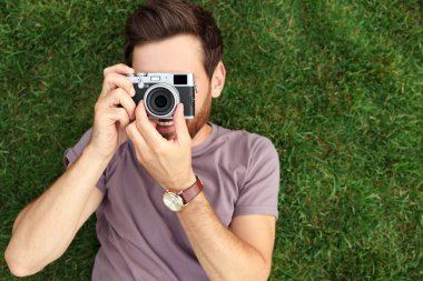 Kameralı bir adam yeşil çimlerin üzerinde fotoğraf çekiyor. İlginç bir hobi.