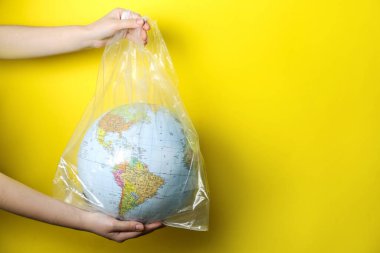 Sarı arka planda plastik torba içinde dünyayı tutan kadın, yakın plan. Mesaj için yer var. Çevresel koruma