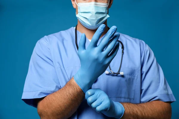 Dokter Beschermende Masker Zetten Medische Handschoenen Tegen Blauwe Achtergrond Close — Stockfoto