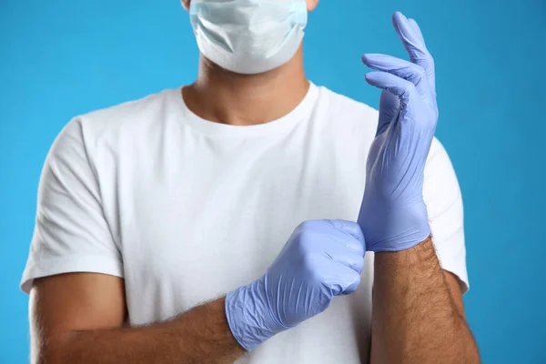 Man Skyddande Ansiktsmask Sätta Medicinska Handskar Mot Blå Bakgrund Närbild — Stockfoto