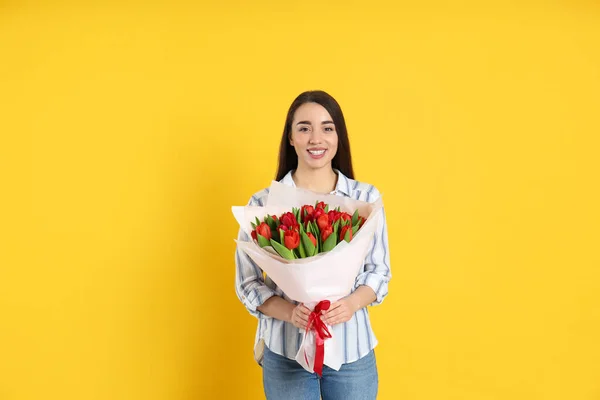 黄色の背景に赤いチューリップの花束を持つ幸せな女性 3月8日 — ストック写真