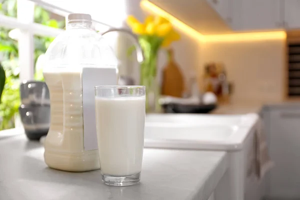 Gallon bottle of milk and glass on white countertop in kitchen. Space for text