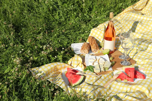 Picnic blanket with delicious food and wine on green grass outdoors, space for text