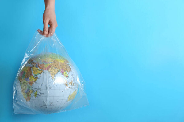 Woman holding plastic bag with globe and space for text on turquoise background, closeup. Environmental conservation