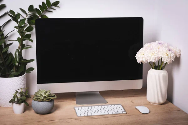 Comfortable workplace with modern computer, green houseplants and beautiful flowers on wooden table indoors