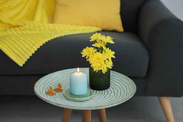 Side table with candle, flowers and earrings near sofa in room. Interior design