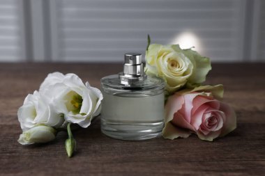 Bir şişe parfüm ve çiçekler ahşap masada.