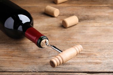 Opening wine bottle with corkscrew on wooden table, closeup. Space for text