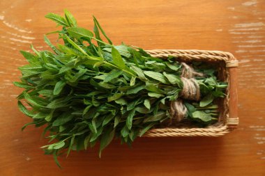 Bunches of beautiful green mint in wicker basket on brown wooden table, top view