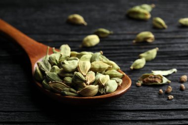 Spoon with dry cardamom pods on black wooden table, closeup