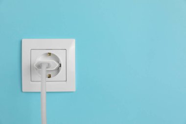 Açık mavi duvardaki güç prizine bağlı şarj adaptörü, metin için boşluk. Elektrik arzı