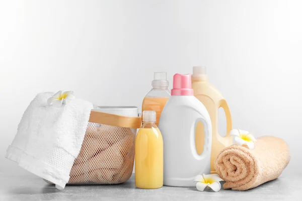 Bottles of laundry detergents and fresh towels on grey table against white background