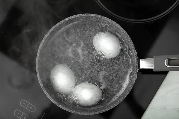 Boiling chicken eggs in saucepan on electric stove, top view