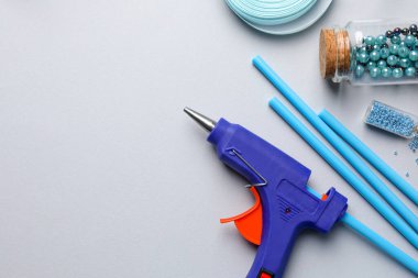 Sıcak tutkal tabancası ve el işi malzemesi gri arka planda, düz yerde. Metin için boşluk