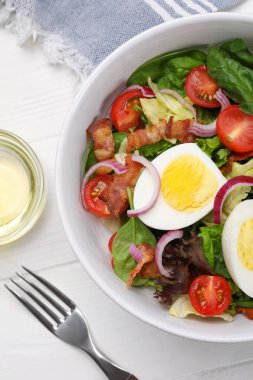 Delicious salad with boiled egg, bacon and vegetables served on white wooden table, flat lay
