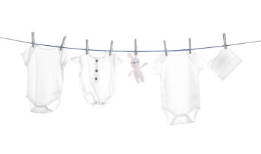 Different baby clothes and toy drying on laundry line against white background