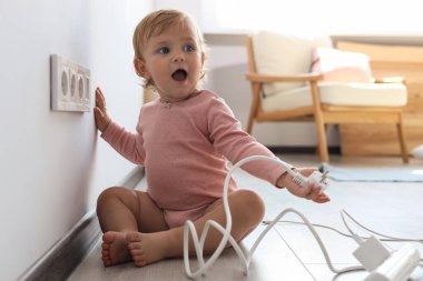 Cute baby playing with electrical socket and plug at home. Dangerous situation