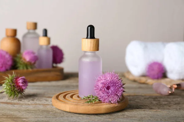 Bottles of herbal essential oil and flowers on wooden table