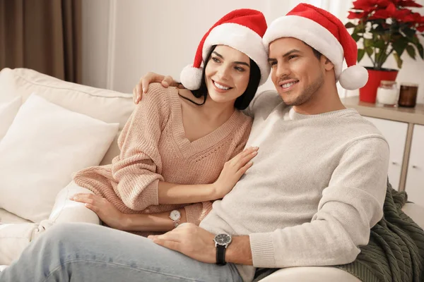 リビングでソファに座っているサンタの帽子の幸せなカップル クリスマスのお祝い — ストック写真