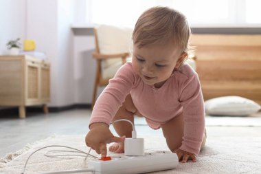 Evde yerde enerji bandıyla oynayan şirin bir bebek. Tehlikeli bir durum.