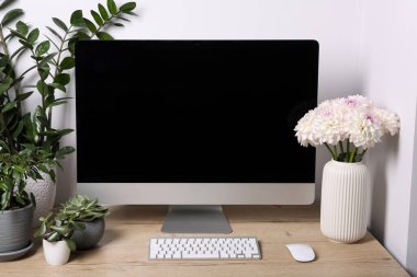 Comfortable workplace with modern computer, green houseplants and beautiful flowers on wooden table indoors