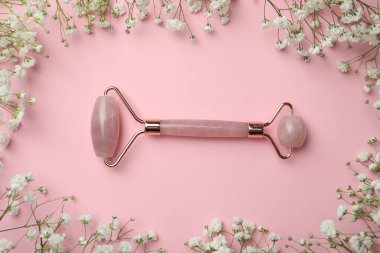 Natural face roller and flowers on pink background, flat lay