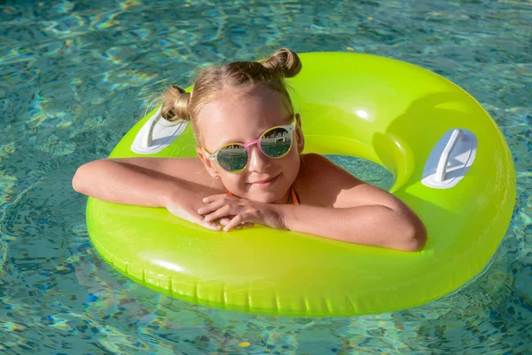 Happy little girl with inflatable ring in outdoor swimming pool on sunny day