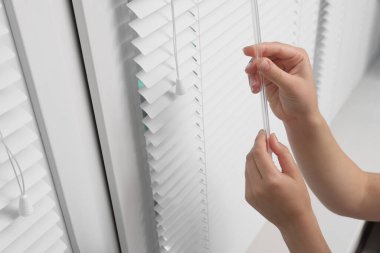 Kadın pencerenin içinde yatay perdeler açıyor, yakın plan.