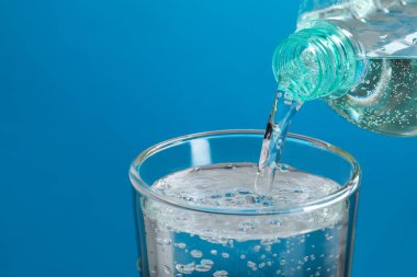 Açık mavi arka planda şişeden cama soda dökmek, yakın plan. Metin için boşluk