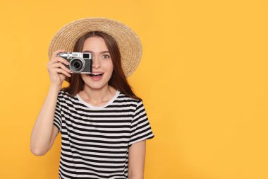 Kameralı genç bir kadın sarı arka planda fotoğraf çekiyor, mesaj için yer var. İlginç bir hobi.
