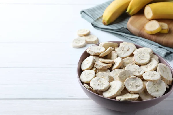 Freeze dried and fresh bananas on white wooden table. Space for text