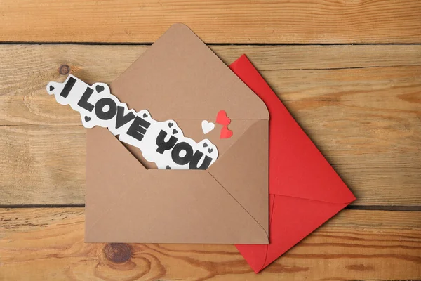 Sheet of paper with phrase I Love You and envelopes on wooden table, flat lay