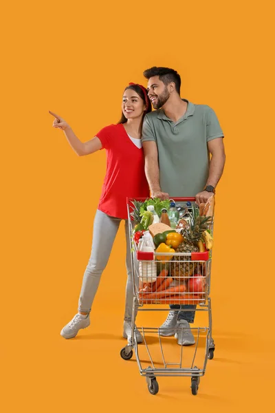 Junges Paar Mit Einkaufswagen Voller Lebensmittel Auf Gelbem Hintergrund — Stockfoto
