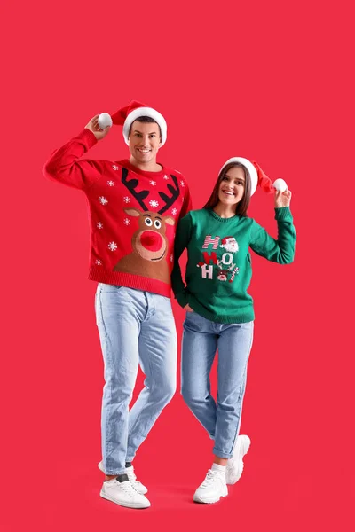 Hermosa Pareja Feliz Sombreros Santa Suéteres Navidad Sobre Fondo Rojo —  Fotos de Stock