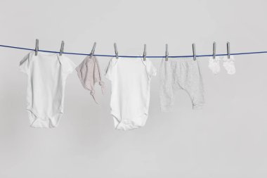 Different baby clothes drying on laundry line against light background