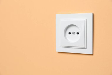Power socket on pale orange wall, space for text. Electrical supply