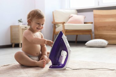 Cute baby playing with iron on floor at home. Dangerous situation