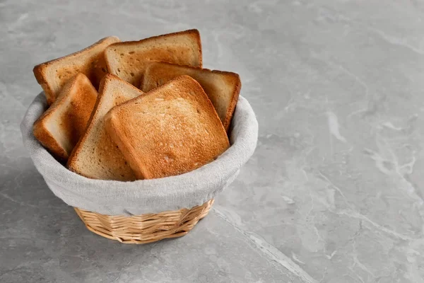 灰色の大理石のテーブルの上においしいトーストパンのスライスとウィッカーバスケット — ストック写真
