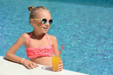Güneşli bir günde havuzda bir bardak meyve suyu içen tatlı küçük bir kız. Metin için boşluk