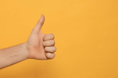Man showing thumb up on orange background, closeup. Space for text