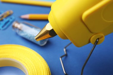 Sıcak tutkal tabancası ve el işi malzemesi mavi masada, yakın plan.