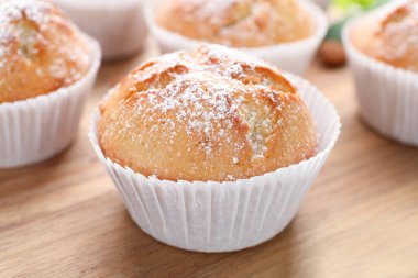 Tasty muffins powdered with sugar on wooden board, closeup