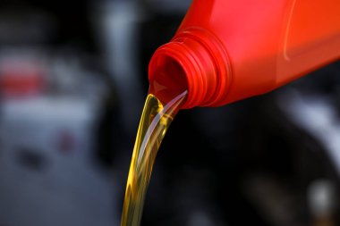 Kırmızı konteynırdan bulanık arka plana motor yağı dökülüyor, yakın plan