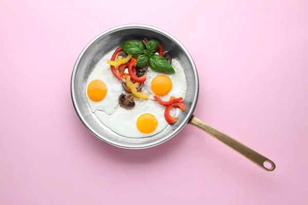 Tasty fried eggs with vegetables in pan on pink background, top view