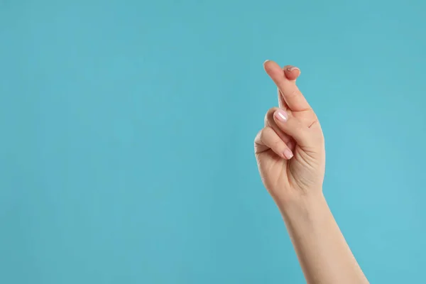 Woman holding fingers crossed on light blue background, closeup with space for text. Good luck superstition