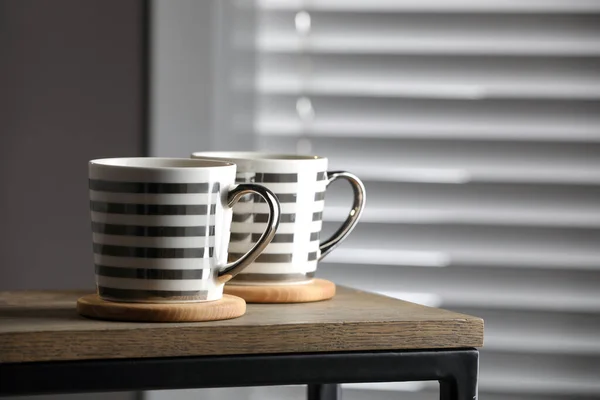 Mugs of drink with stylish cup coasters on wooden table in room. Space for text