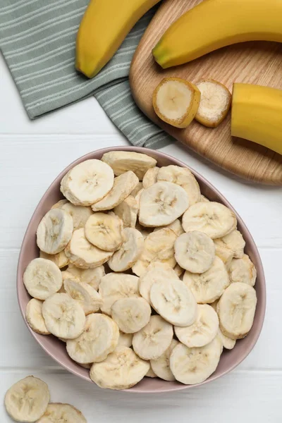 Freeze dried and fresh bananas on white wooden table, flat lay