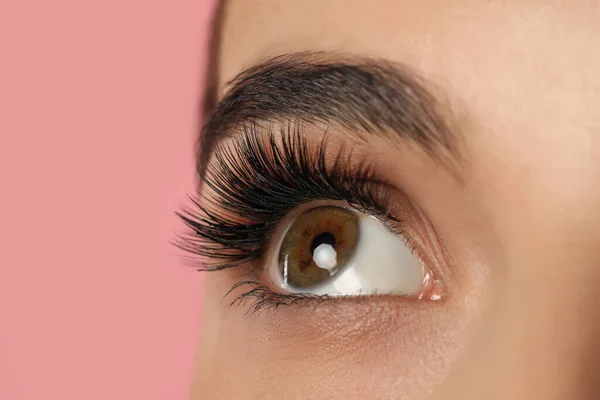 Beautiful young woman with long eyelashes on pink background, closeup